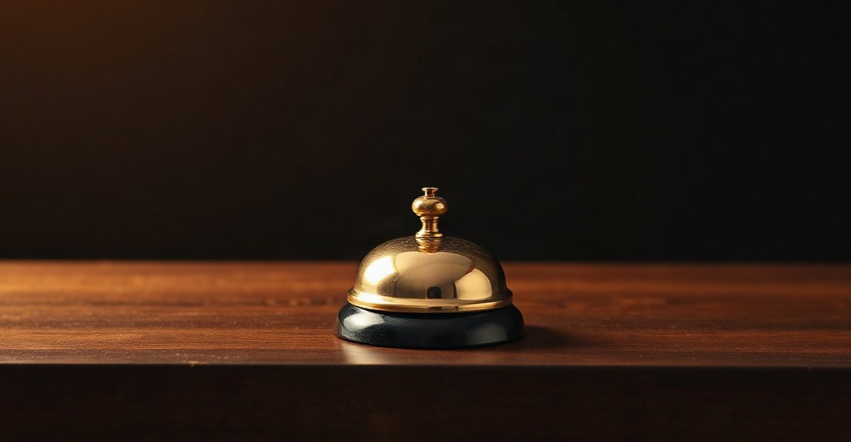 A single brass desk bell on a dark counter lit by a warm amber light
